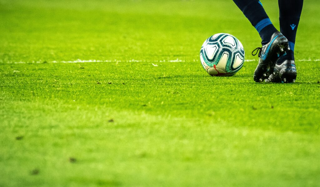 A pair of legs and a football on a pitch