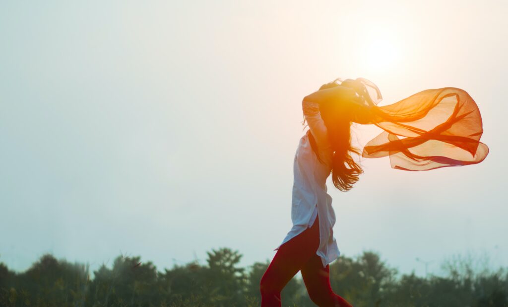 A person standing in an open area, the sun shining behind them, giving a sense of freedom