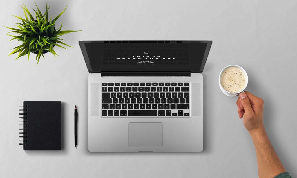 A laptop, diary. a hot drink being picked up by a hand
